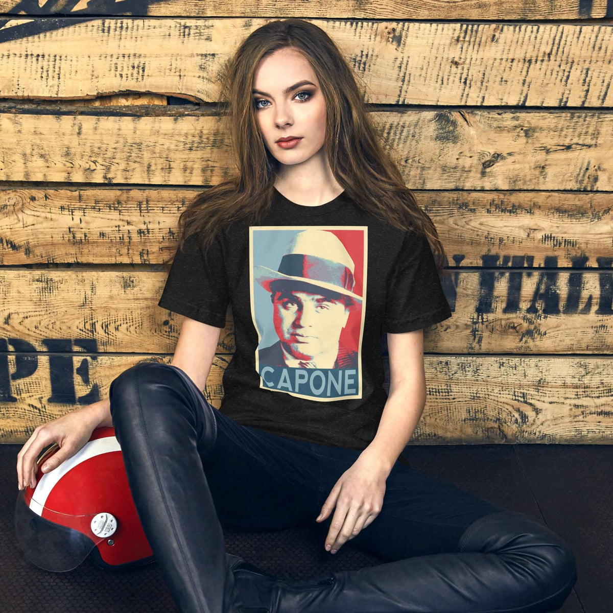 Model wearing a black unisex t-shirt featuring a graphic design inspired by Capone, on a rustic wooden background.